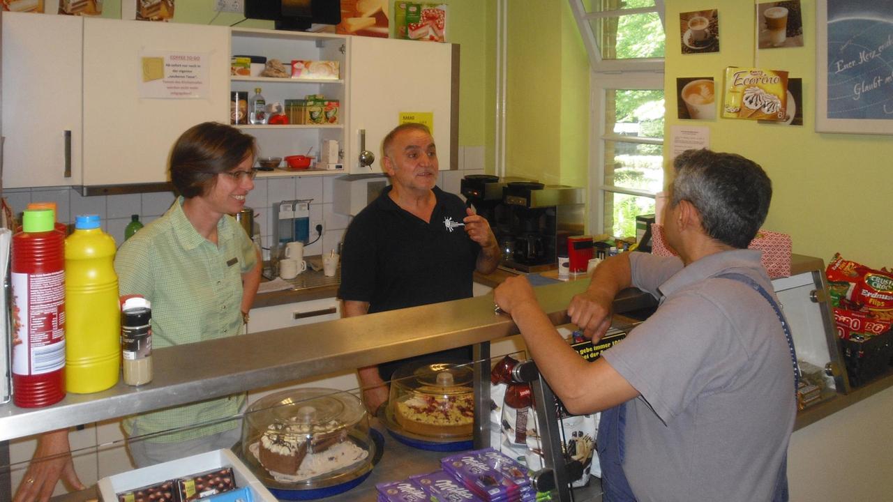 An einem Tresen mit Kuchen und Schokolade stehen drei Personen im Gespräch. An einem Tresen mit Kuchen und Schokolade stehen drei Personen im Gespräch.