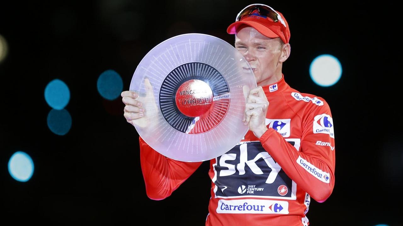 Froome im roten Trikot und mit roter Mütze küsst seine Trophäe: Eine milchglasige Scheibe. Der Hintergrund ist dunkel bis auf einige Farbreflexe. Froome im roten Trikot und mit roter Mütze küsst seine Trophäe: Eine milchglasige Scheibe. Der Hintergrund ist dunkel bis auf einige Farbreflexe.