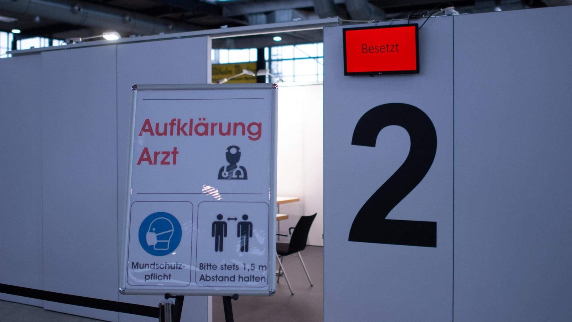In einer Halle, die zu einem Corona-Impfzentrum umfunktioniert wird, sind Trennwände aufgebaut. Zu sehen ist zudem ein Schild mit der Aufschrift "Aufklärung Arzt". In einer Halle, die zu einem Corona-Impfzentrum umfunktioniert wird, sind Trennwände aufgebaut. Zu sehen ist zudem ein Schild mit der Aufschrift "Aufklärung Arzt".