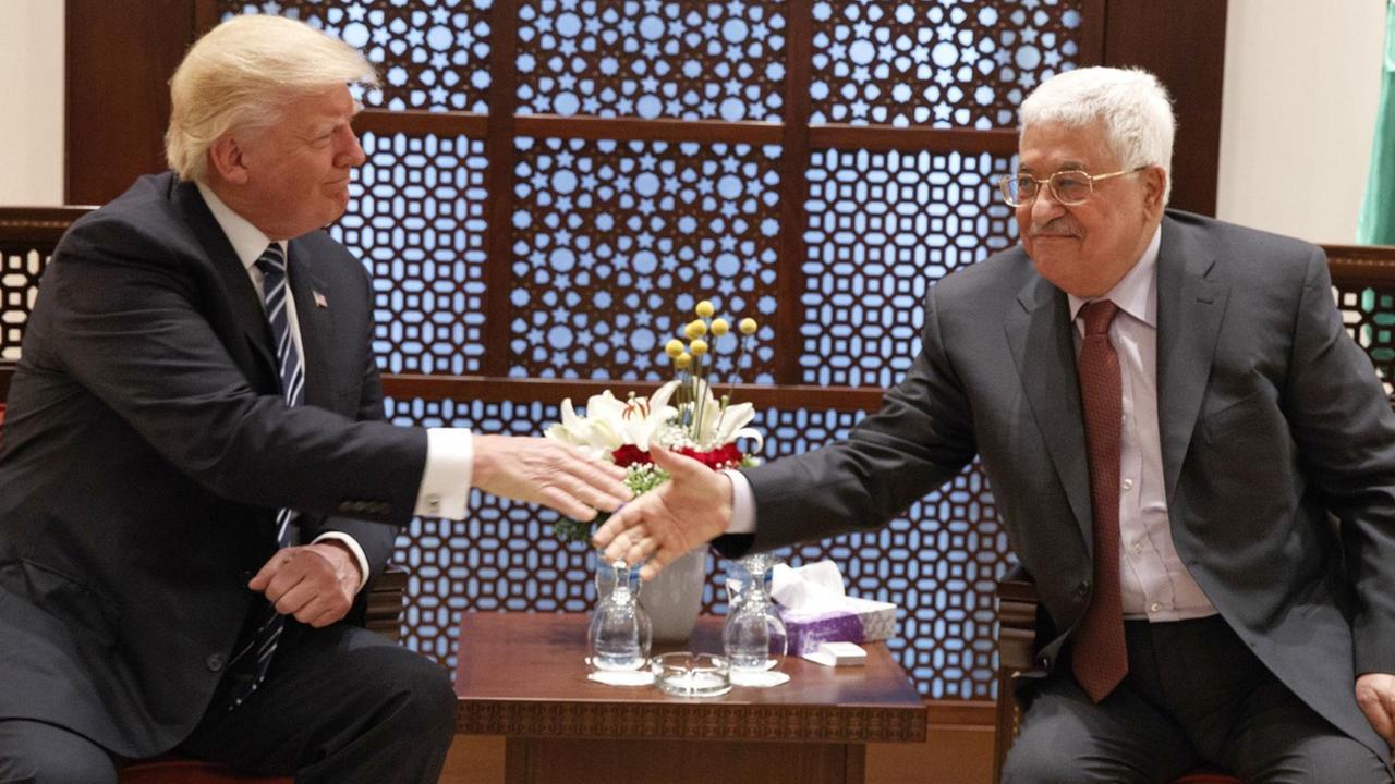 Trump und Abbas sitzen in Sesseln an einem kleinen Tisch und reichen sich lächelnd die Hand. Trump und Abbas sitzen in Sesseln an einem kleinen Tisch und reichen sich lächelnd die Hand.