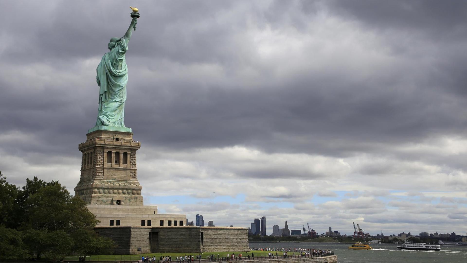 Die Freiheitsstatue auf Liberty Island auf ihrem Sockel, im Hintergrund angedeutet die Skyline von New York