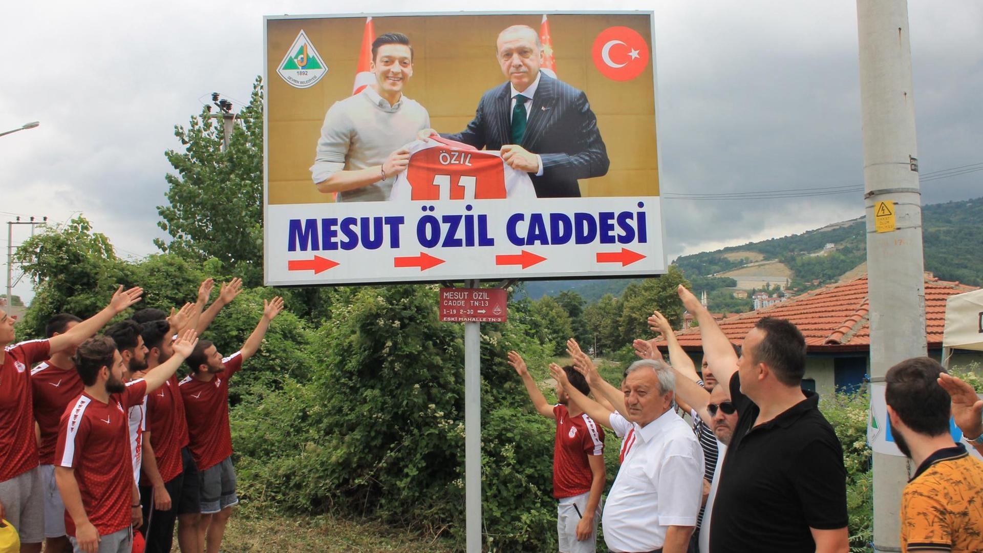 Mehrere Männer auf einer Straße stehen links und rechts neben einem Plakat, das ein gemeinsames Foto von Mesut Özil und dem türkischen Präsidenten Erdogan zeigt. Mehrere Männer auf einer Straße stehen links und rechts neben einem Plakat, das ein gemeinsames Foto von Mesut Özil und dem türkischen Präsidenten Erdogan zeigt.