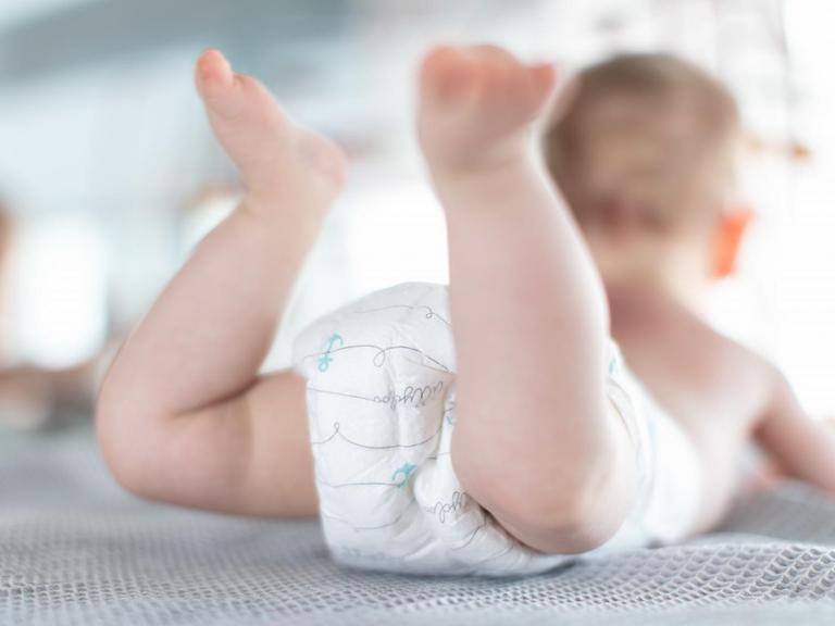 Ein Säugling trägt Pampers, während er auf einer Kommode liegt.