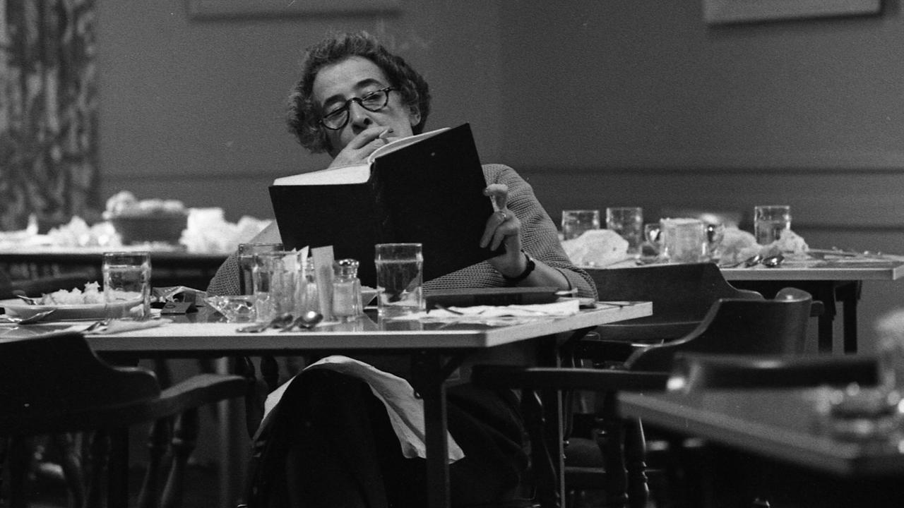 Die Philosophin Hannah Arendt sitzt an einem Tisch in einer Bibliothek, liest und raucht. Die Philosophin Hannah Arendt sitzt an einem Tisch in einer Bibliothek, liest und raucht.