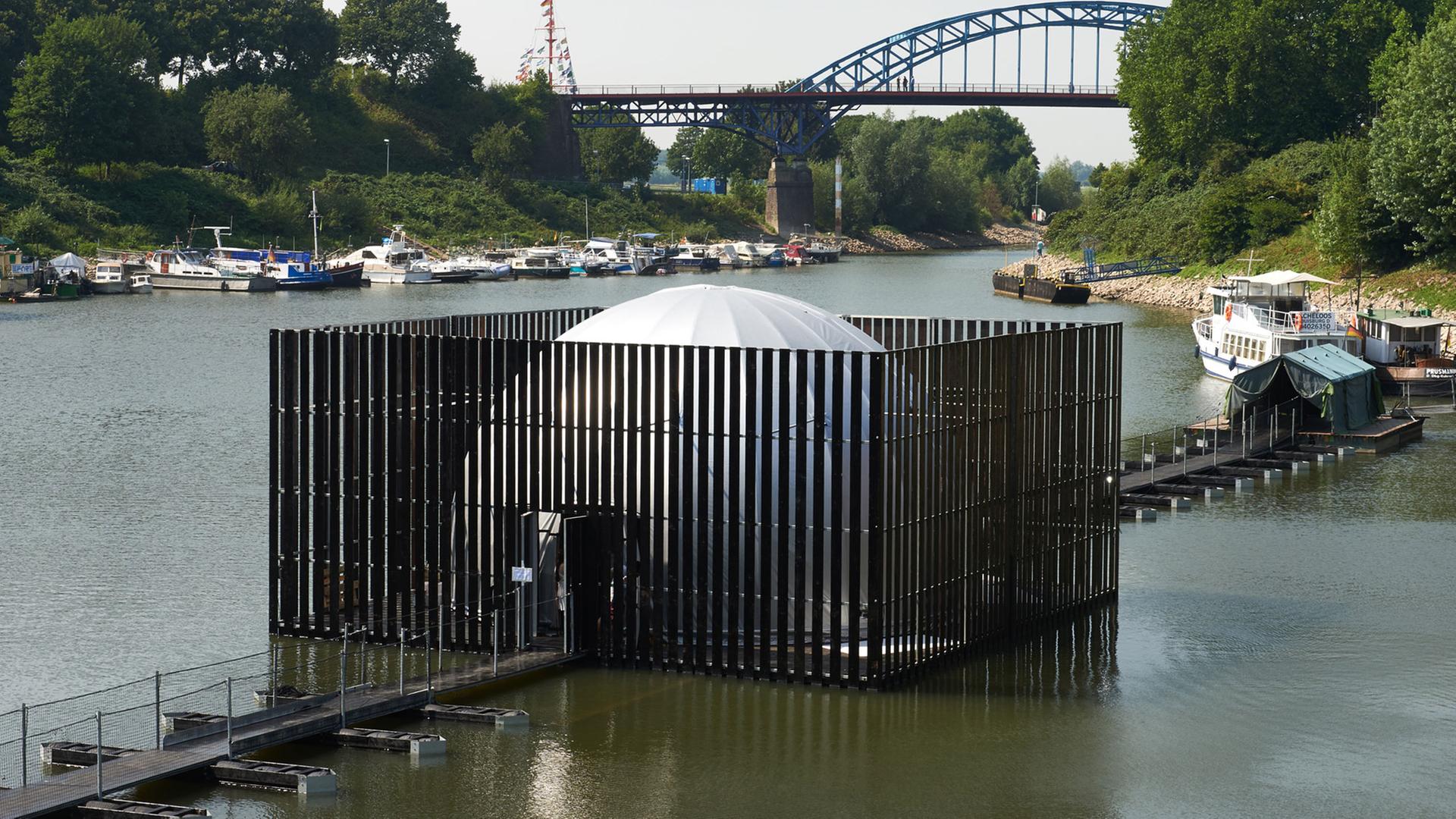 Die Installation "Nomanslanding" im ehemaligen Eisenbahnhafen in Duisburg-Ruhrort. Sie umfasst zwei große, bewegliche Plattformen, die sich auf der Wasserfläche allmählich zu einem Dom in Form einer Halbkugel vereinigen. 