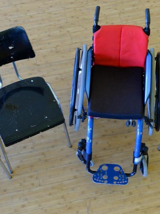 Ein Rollstuhl steht in einer Schule zwischen anderen Stühlen. |