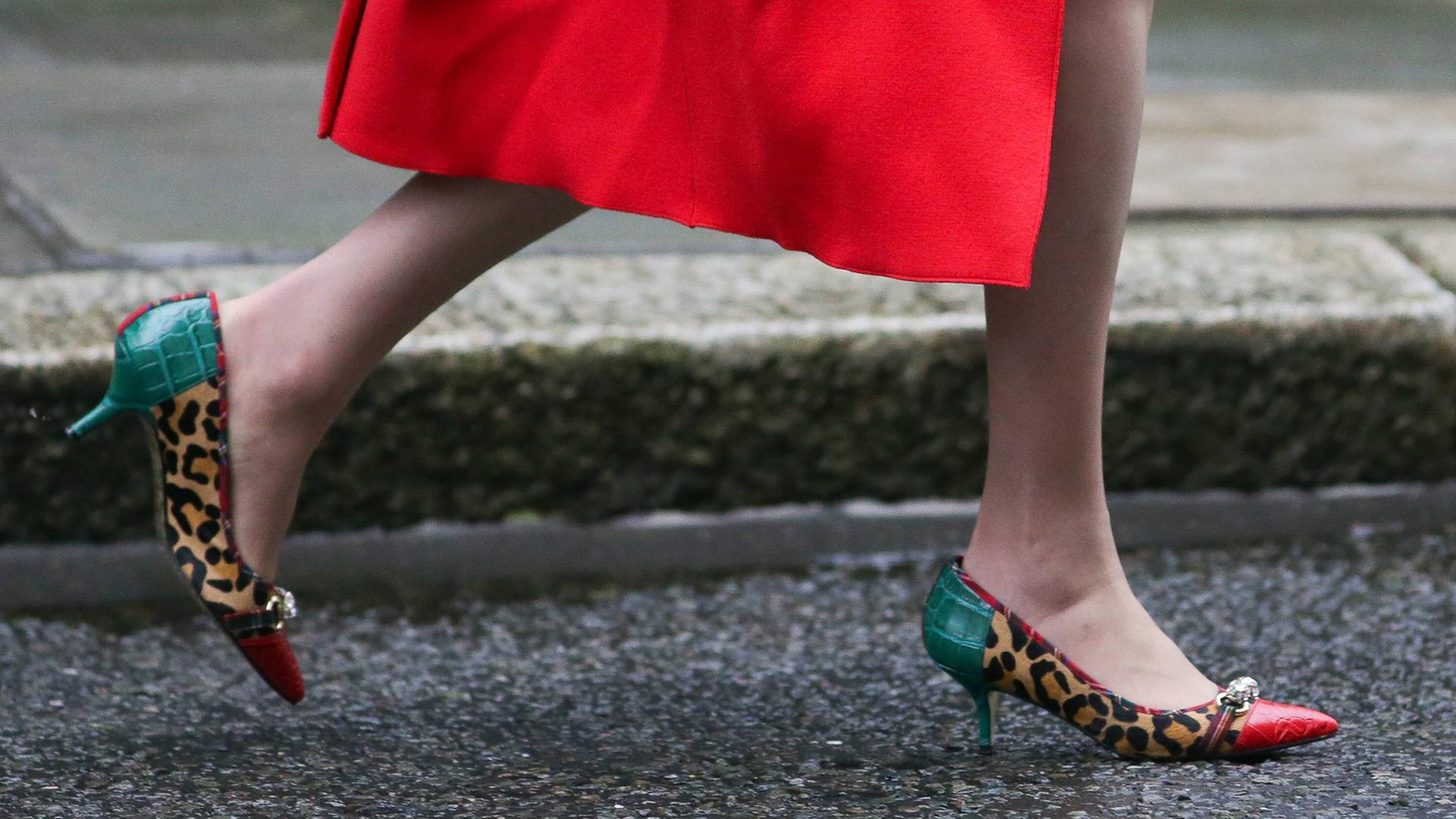 Man sieht die Beine einer Frau, die in bunten High Heels auf dem Asphalt läuft. Man sieht die Beine einer Frau, die in bunten High Heels auf dem Asphalt läuft.