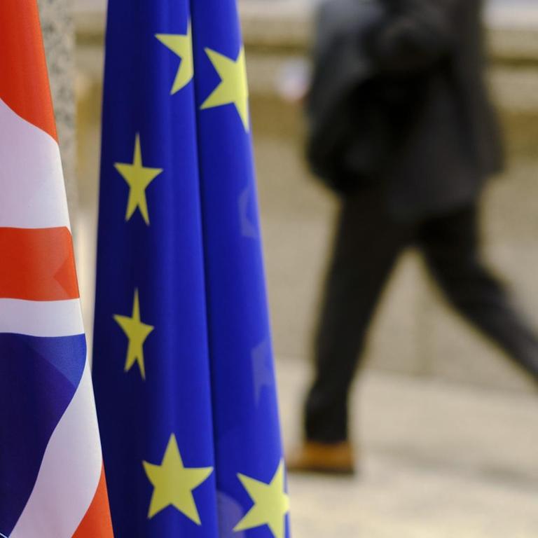 The flags of Great Britain and the EU side by side in the foreground, in the background a man walking down the street