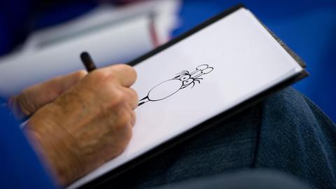 Der argentinische Zeichner Guillermo Mordillo ist am 13.10.2012 zu Gast auf dem sogenannten Blauen Sofa auf der Buchmesse in Frankfurt am Main und zeichnet eine Giraffe. Zu sehen ist seine Hand, die auf einen Blatt Papier eine Zeichnung anfertig. Mordillo stellte sein Buch "4 x 20 Jahre jung" vor.