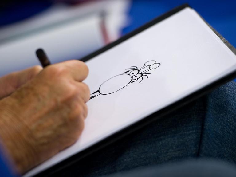 Der argentinische Zeichner Guillermo Mordillo ist am 13.10.2012 zu Gast auf dem sogenannten Blauen Sofa auf der Buchmesse in Frankfurt am Main und zeichnet eine Giraffe. Zu sehen ist seine Hand, die auf einen Blatt Papier eine Zeichnung anfertig. Mordillo stellte sein Buch "4 x 20 Jahre jung" vor.
