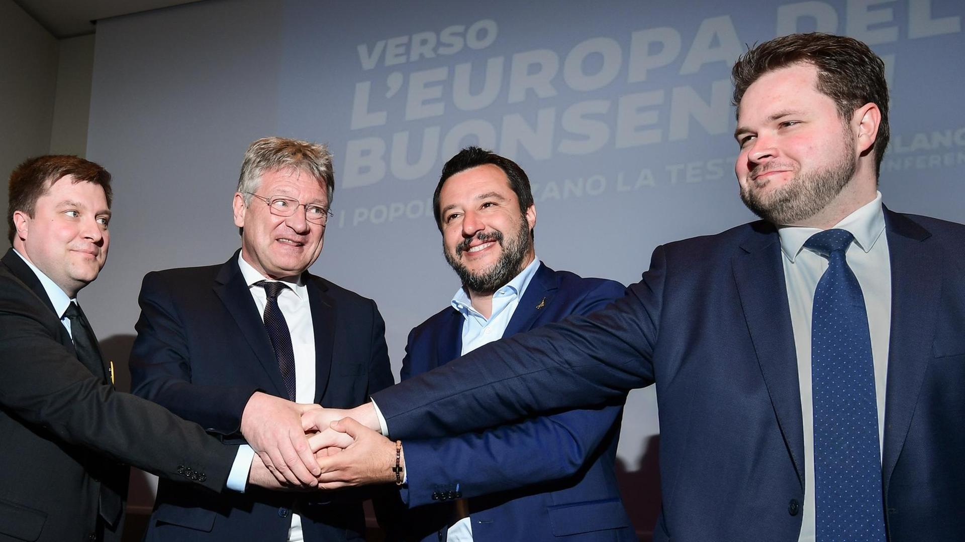Die vier Politiker legen die Hände ineinander und lächeln in die Kamera Die vier Politiker legen die Hände ineinander und lächeln in die Kamera