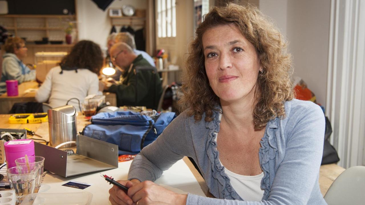 Martine Postma agiert seit 2009 als Gründerin der Repair-Café-Bewegung. Mittellange, lockige Haare. Sie sitzt in Amsterdam in einem Repair-Café. Martine Postma agiert seit 2009 als Gründerin der Repair-Café-Bewegung. Mittellange, lockige Haare. Sie sitzt in Amsterdam in einem Repair-Café.