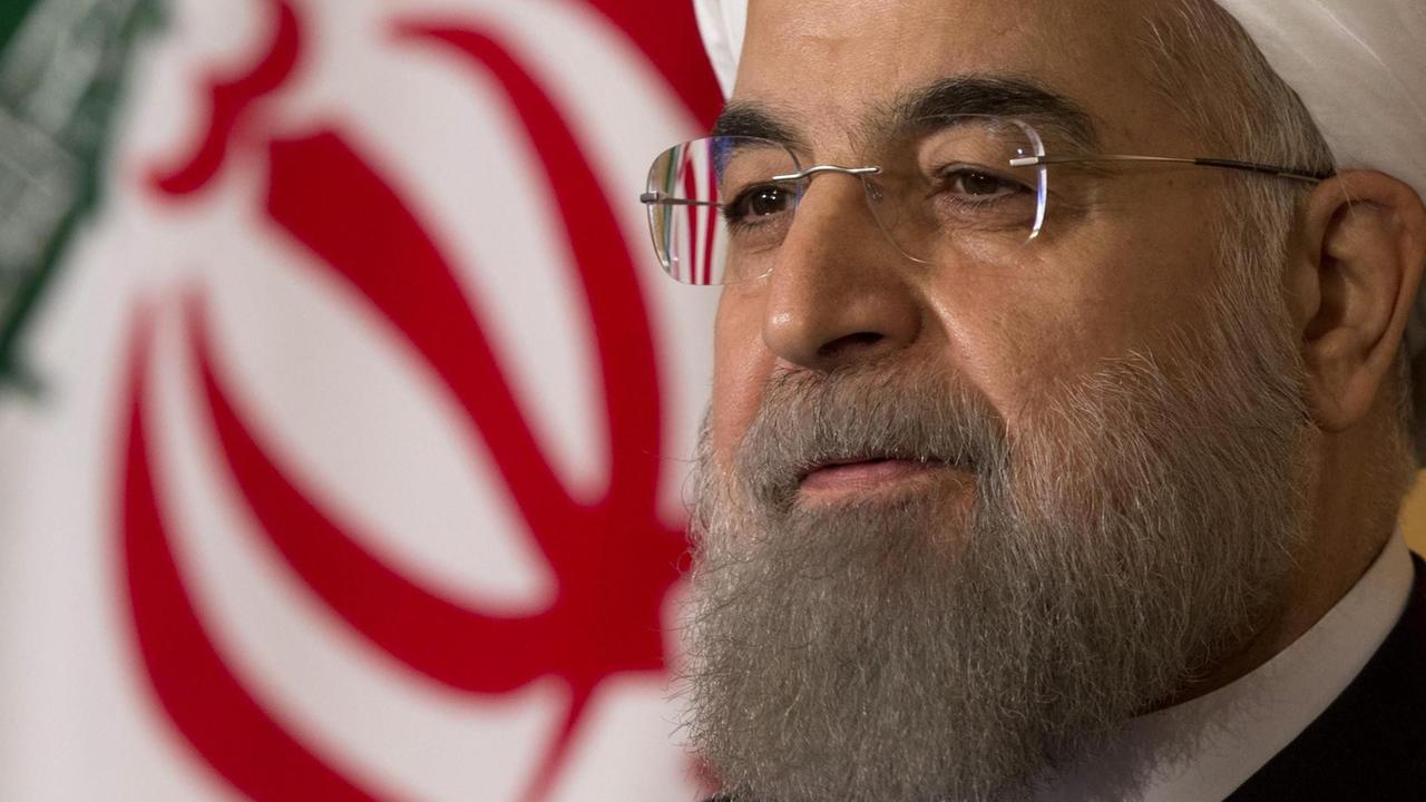 Rohani trägt einen weißen Turban und Brille. Hinter ihm sieht man einen teil der iranischen Nationalflagge. Rohani trägt einen weißen Turban und Brille. Hinter ihm sieht man einen teil der iranischen Nationalflagge.