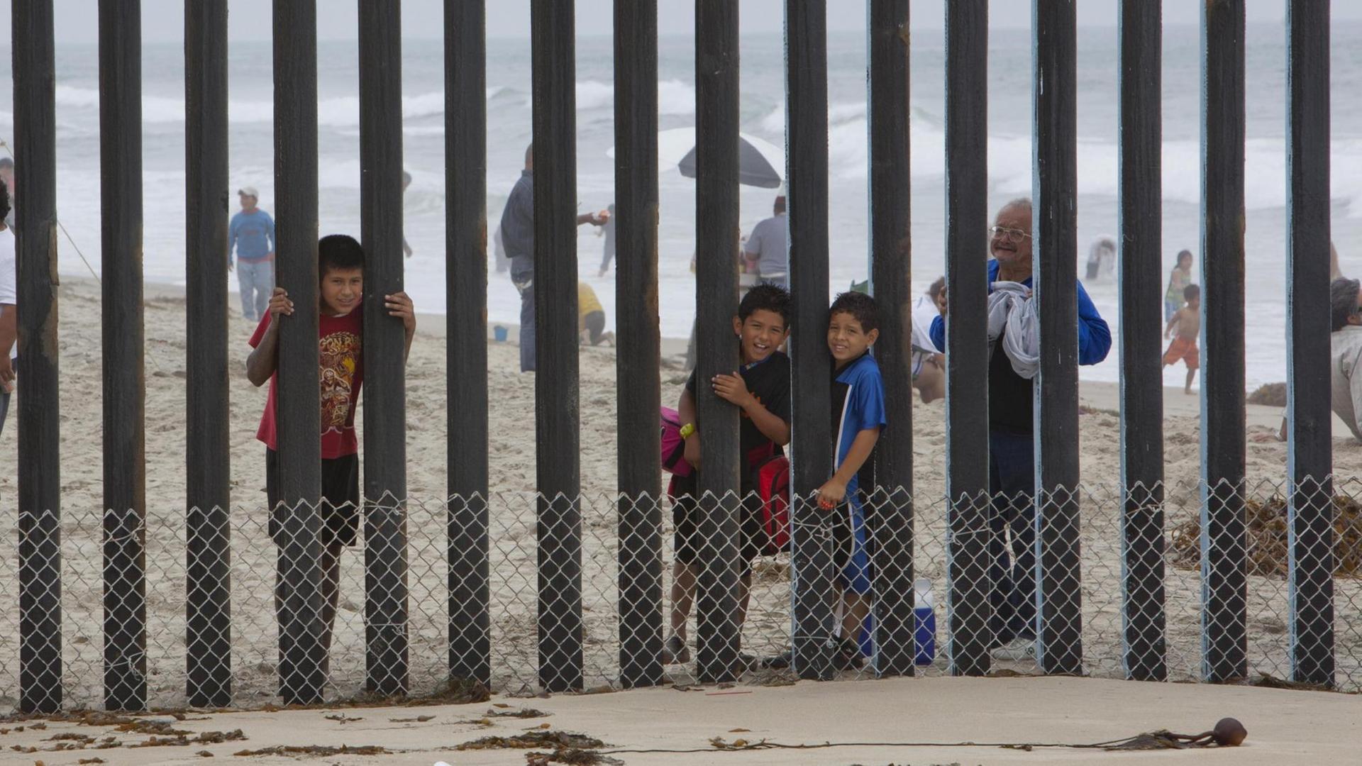 Kinder schauen durch einen Zaun von Mexiko in die USA.
