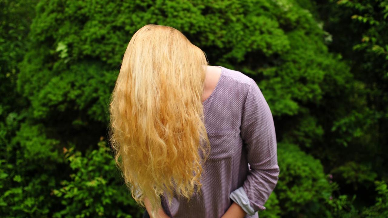 Das Bild zeigt eine blonde Frau, deren Gesicht gänzlich durch ihr Haar verdeckt wird Das Bild zeigt eine blonde Frau, deren Gesicht gänzlich durch ihr Haar verdeckt wird