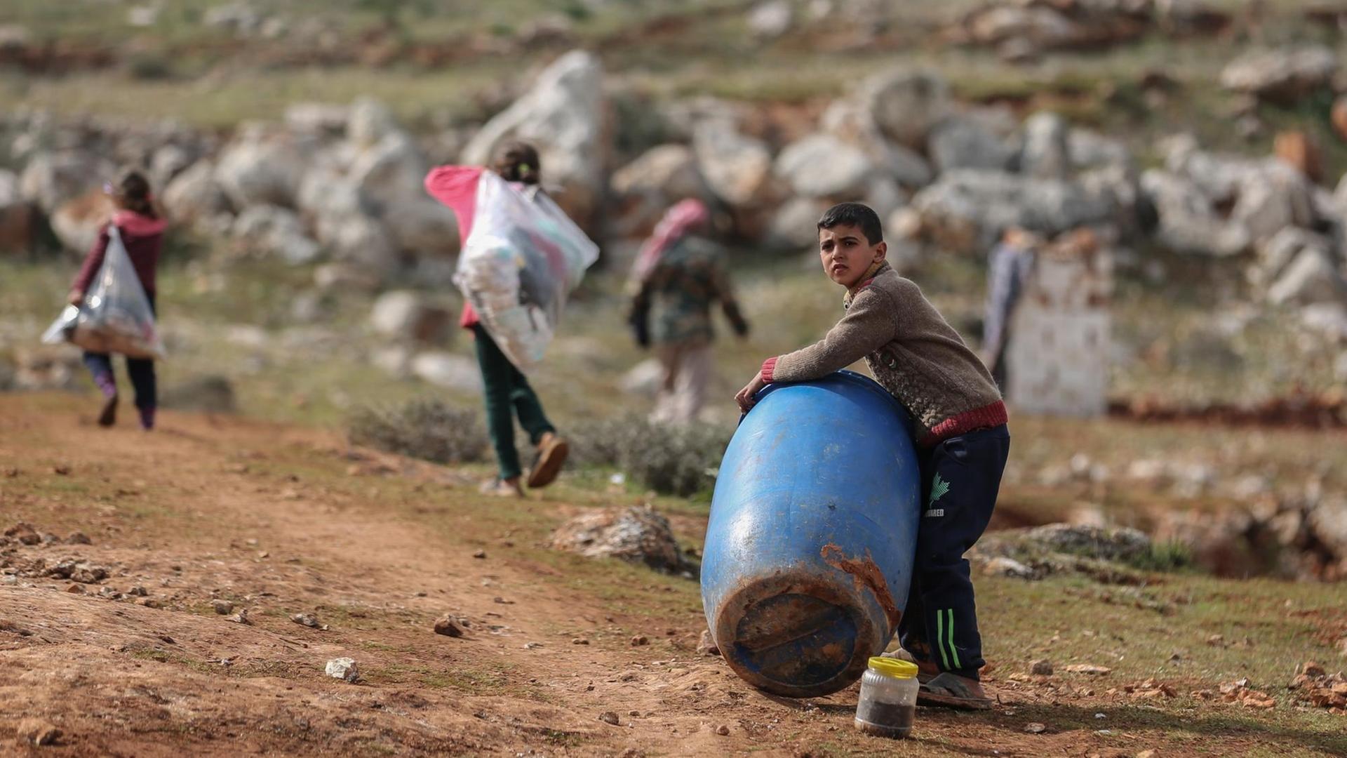 Ein syrischer Junge hält ein Plastikfass in der Nähe eines behelfsmäßigen Lagers für Familien, die infolge der Bombardierung und der Militäroperationen aus dem Idlib-Land vertrieben wurden. Ein syrischer Junge hält ein Plastikfass in der Nähe eines behelfsmäßigen Lagers für Familien, die infolge der Bombardierung und der Militäroperationen aus dem Idlib-Land vertrieben wurden.