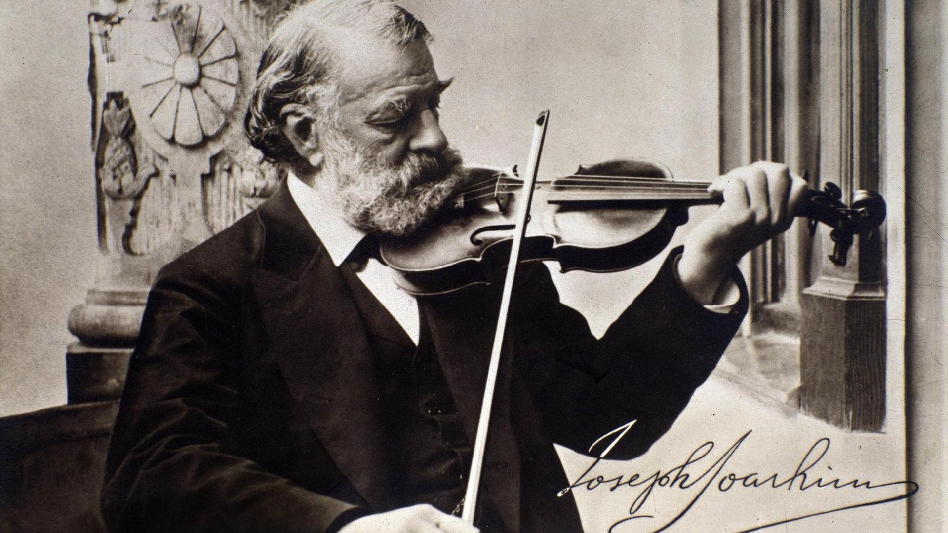 Schwarz-weiß Foto, aufgenommen um 1900, mit dem spielenden Geiger Joseph Joachim, er trägt einen scharzen Anzug und schaut auf das Griffbrett, er trägt einen weißen Vollbart und hat weiße Haare, unten rechts ist seine Unterschrift verzeichnet Schwarz-weiß Foto, aufgenommen um 1900, mit dem spielenden Geiger Joseph Joachim, er trägt einen scharzen Anzug und schaut auf das Griffbrett, er trägt einen weißen Vollbart und hat weiße Haare, unten rechts ist seine Unterschrift verzeichnet