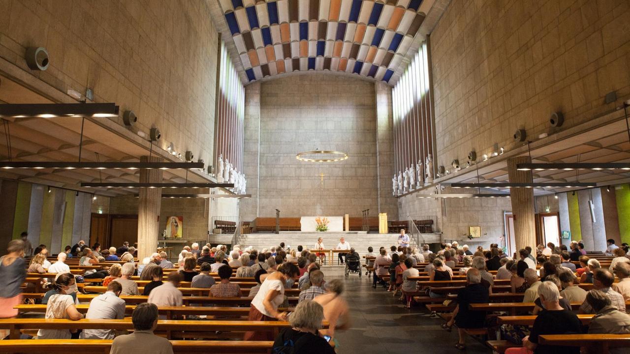Altarraum einer modernen Kirche. Die Kirchenbänke sind gut gefüllt, vorne ein Tisch, hinter dem die Podiumsteilnehmer sitzen. Altarraum einer modernen Kirche. Die Kirchenbänke sind gut gefüllt, vorne ein Tisch, hinter dem die Podiumsteilnehmer sitzen.