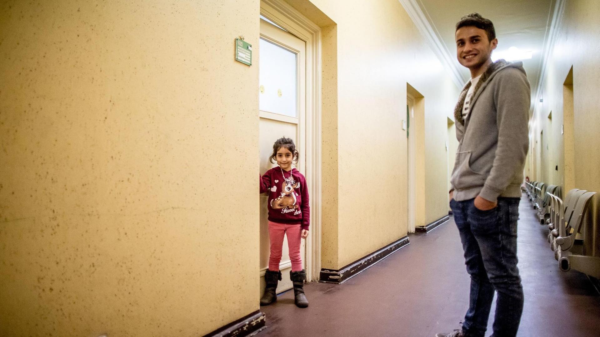 Farbfoto von zwei Personen, die in einem Hausflur stehen und in die Kamera lächeln. Es sind ein kleines ca. siebenjähriges Mädchen und ihr erwachsener Bruder, Flüchtlinge aus Syrien.