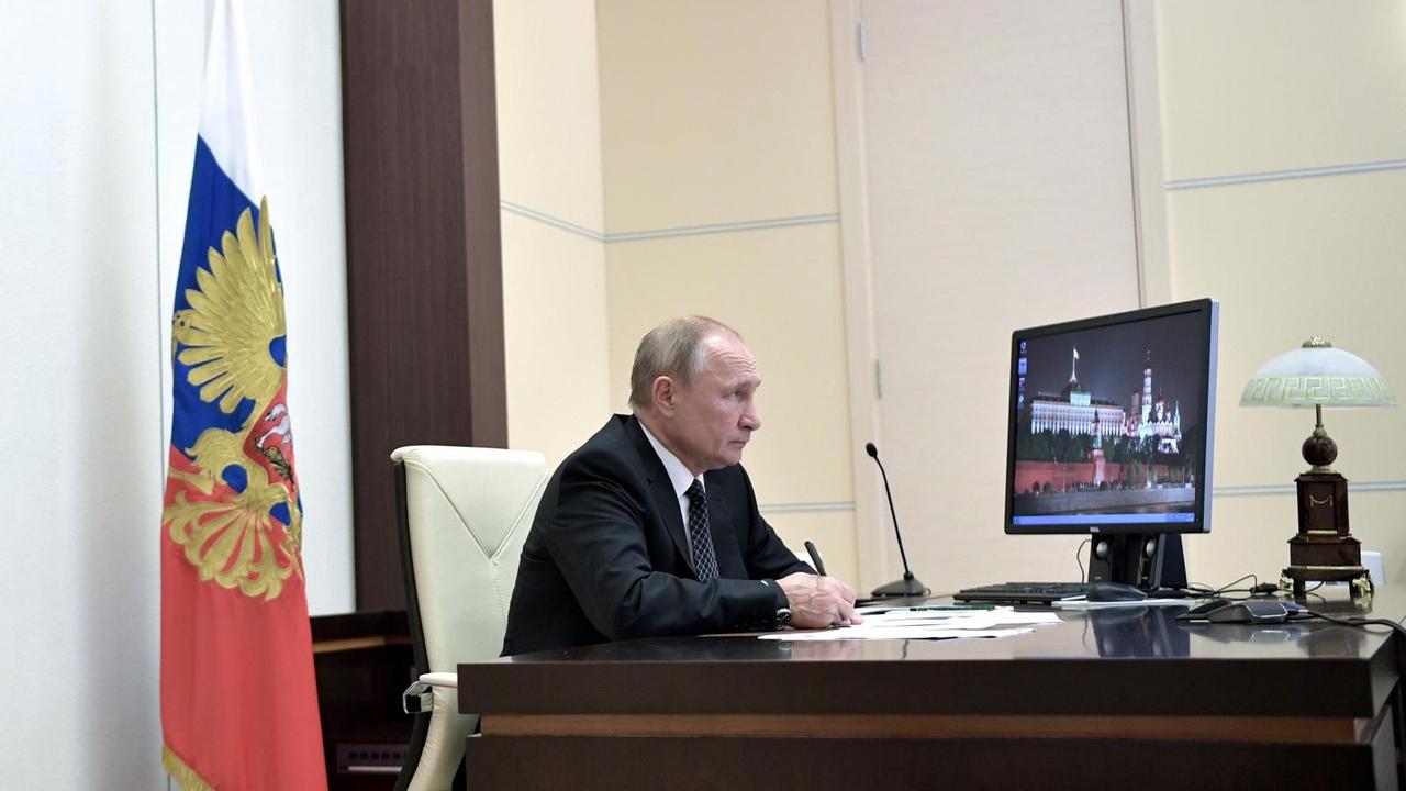 Wladimir Putin sitz an seinem Schreibtisch vor einem Computermonitor, auf dem ein Bild des Kremls zu sehen ist. Wladimir Putin sitz an seinem Schreibtisch vor einem Computermonitor, auf dem ein Bild des Kremls zu sehen ist.