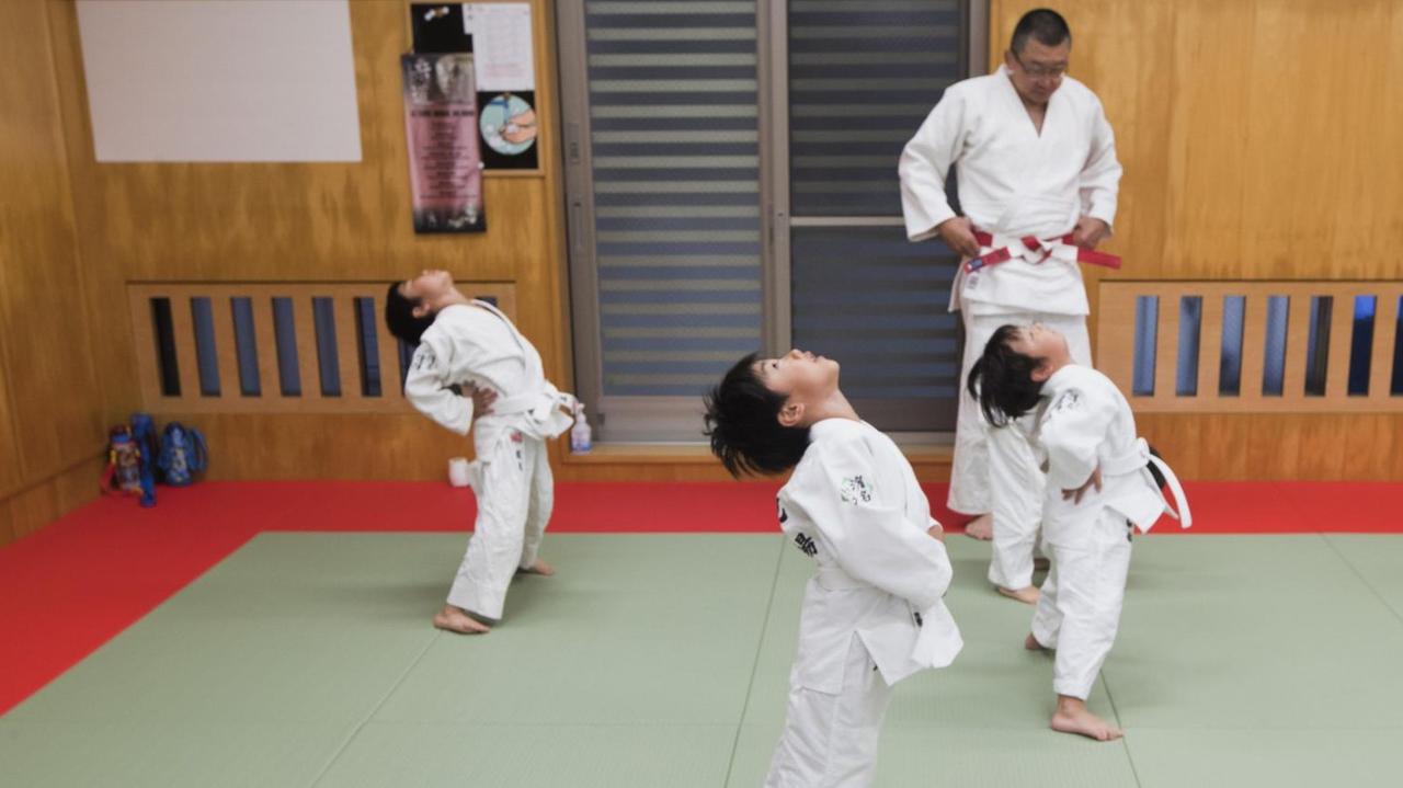 Judotraining: Kinder stehen in einer Sporthalle und dehnen ihren Rücken. Judotraining: Kinder stehen in einer Sporthalle und dehnen ihren Rücken.