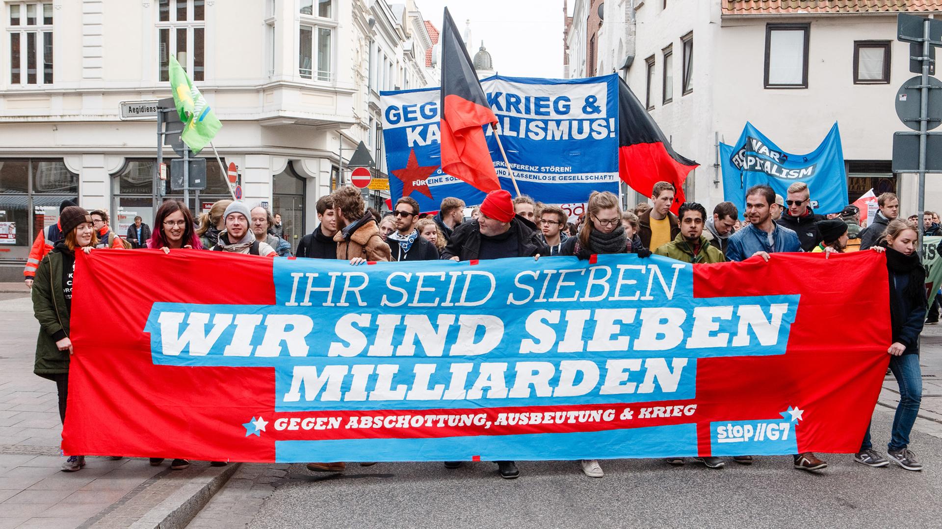 Demonstranten ziehen am 14.04.2015 in Lübeck (Schleswig-Holstein) auf der zentralen Demonstration des Bündnisses Stop G7 mit einem Transparent mit der Aufschrift "Ihr seid sieben. Wir sind sieben Milliarden" durch die Hansestadt.
