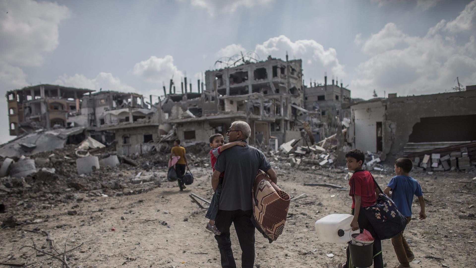 Ein Mann und seine Söhne sind auf dem Weg nach Hause, im Hintergrund sieht man zerstörte Häuser im Gazastreifen. Ein Mann und seine Söhne sind auf dem Weg nach Hause, im Hintergrund sieht man zerstörte Häuser im Gazastreifen.
