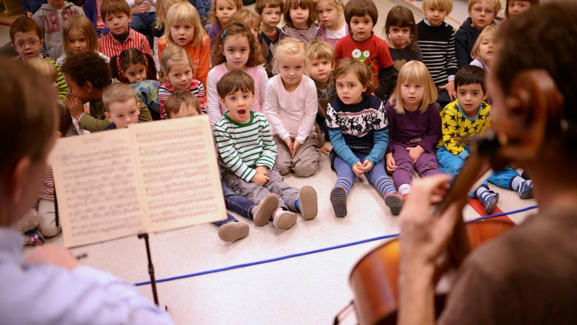 Kinder sitzen singend zwei Cellisten gegenüber. Kinder sitzen singend zwei Cellisten gegenüber.