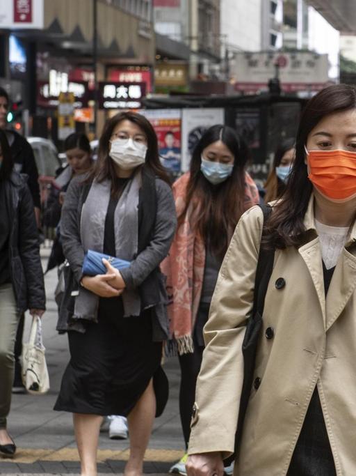 Menschen mit Mund-Nasen-Schutz auf einer Geschäftsmeile in Hongkong