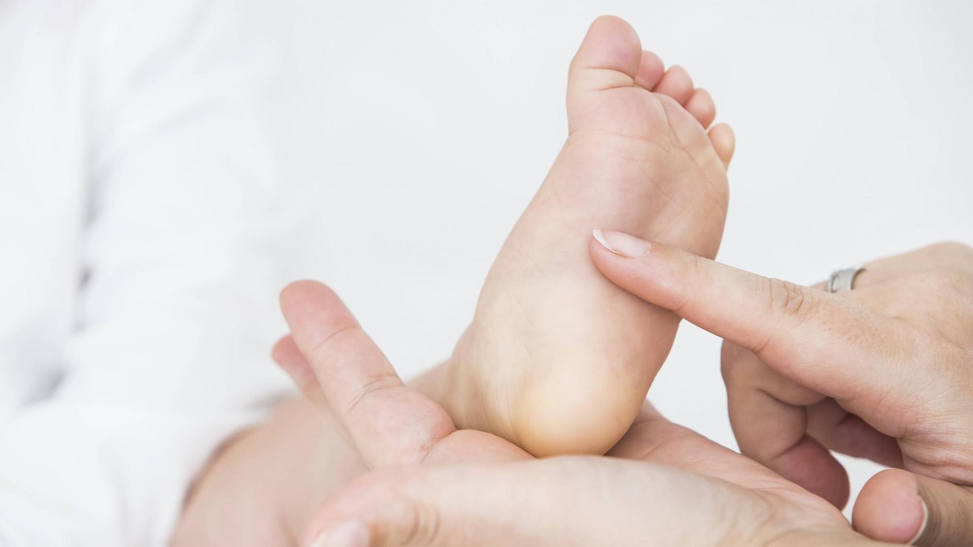 Die Hand einer Mutter kitzelt die Fußsohle ihres Babys.