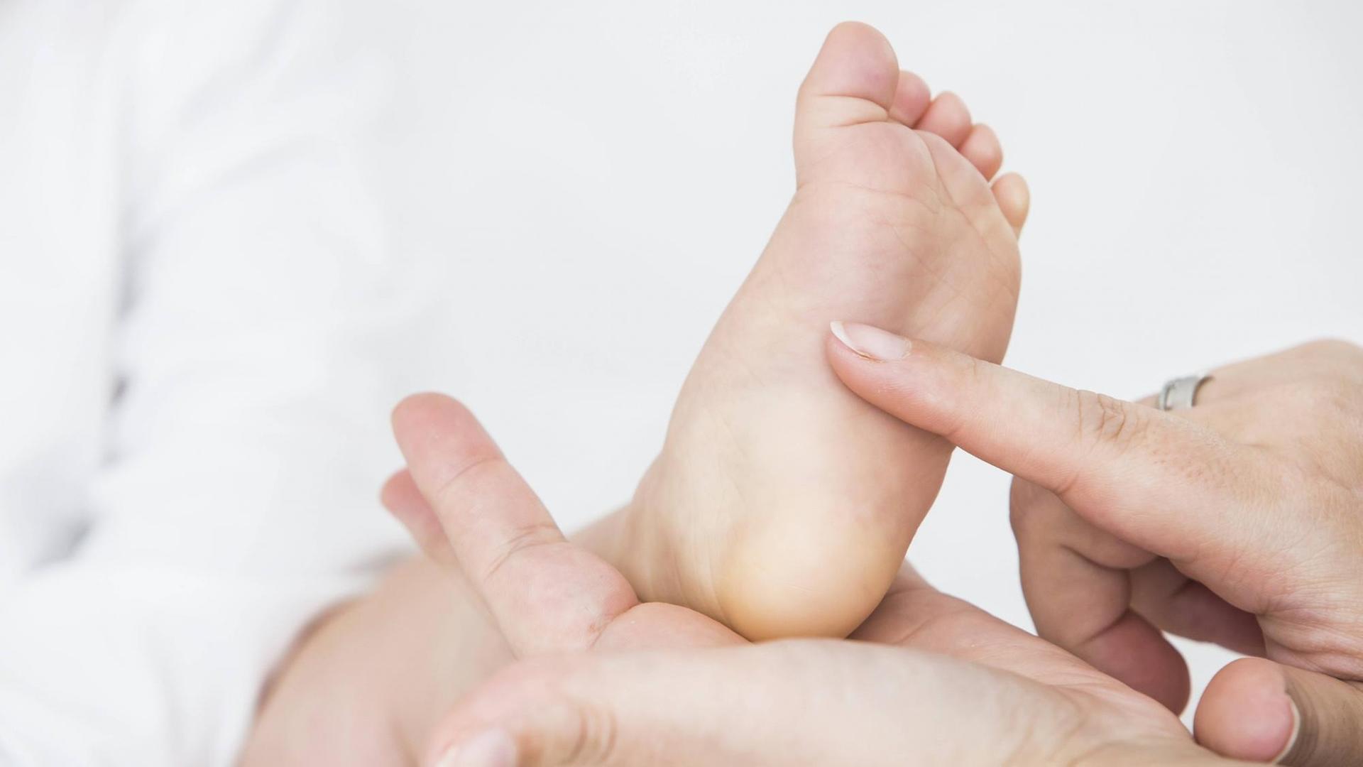 Die Hand einer Mutter kitzelt die Fußsohle ihres Babys. Die Hand einer Mutter kitzelt die Fußsohle ihres Babys.
