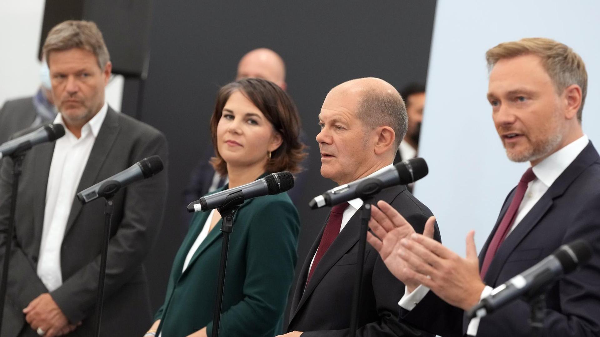 Vier Politiker stehen an Mikrofonen. Vier Politiker stehen an Mikrofonen.