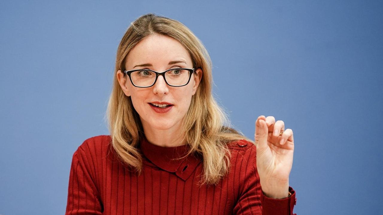 Eine blonde Frau mit eckiger Brille gestikuliert fein beim Reden. Sie trägt Eine blonde Frau mit eckiger Brille gestikuliert fein beim Reden. Sie trägt