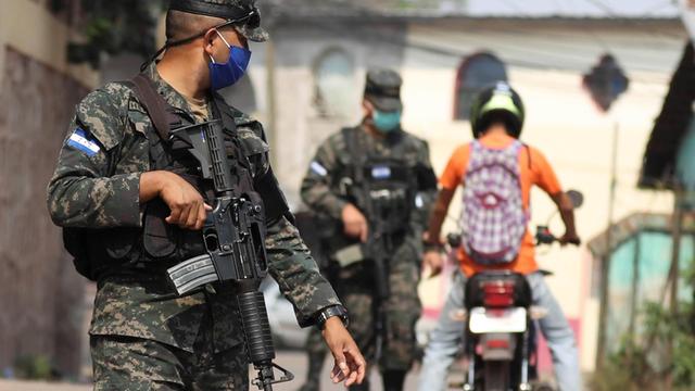Soldaten mit Maschinengewehr und Mundschutz kontrollieren Passanten in Tegucigalpa, Honduras.
