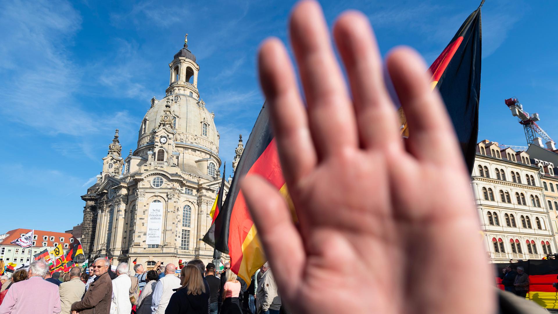 Ein Teilnehmer einer Kundgebung von Pegida auf dem Altmarkt in Dresden hält seine Hand vor die Kamera des Fotografen.