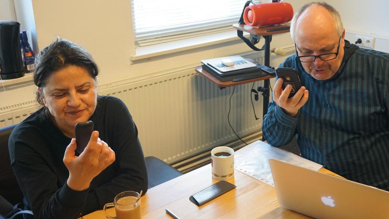Die Mitarbeitenden des Mehrgenerationenhauses Wassertor, Ralf Pierau und Vicdan Avci sitzen am Tisch und halten Smartphones in der Hand. Darüber kommunizieren sie mit Senioren, die wegen Corona nicht mehr in die Einrichtung kommen können. Die Mitarbeitenden des Mehrgenerationenhauses Wassertor, Ralf Pierau und Vicdan Avci sitzen am Tisch und halten Smartphones in der Hand. Darüber kommunizieren sie mit Senioren, die wegen Corona nicht mehr in die Einrichtung kommen können.