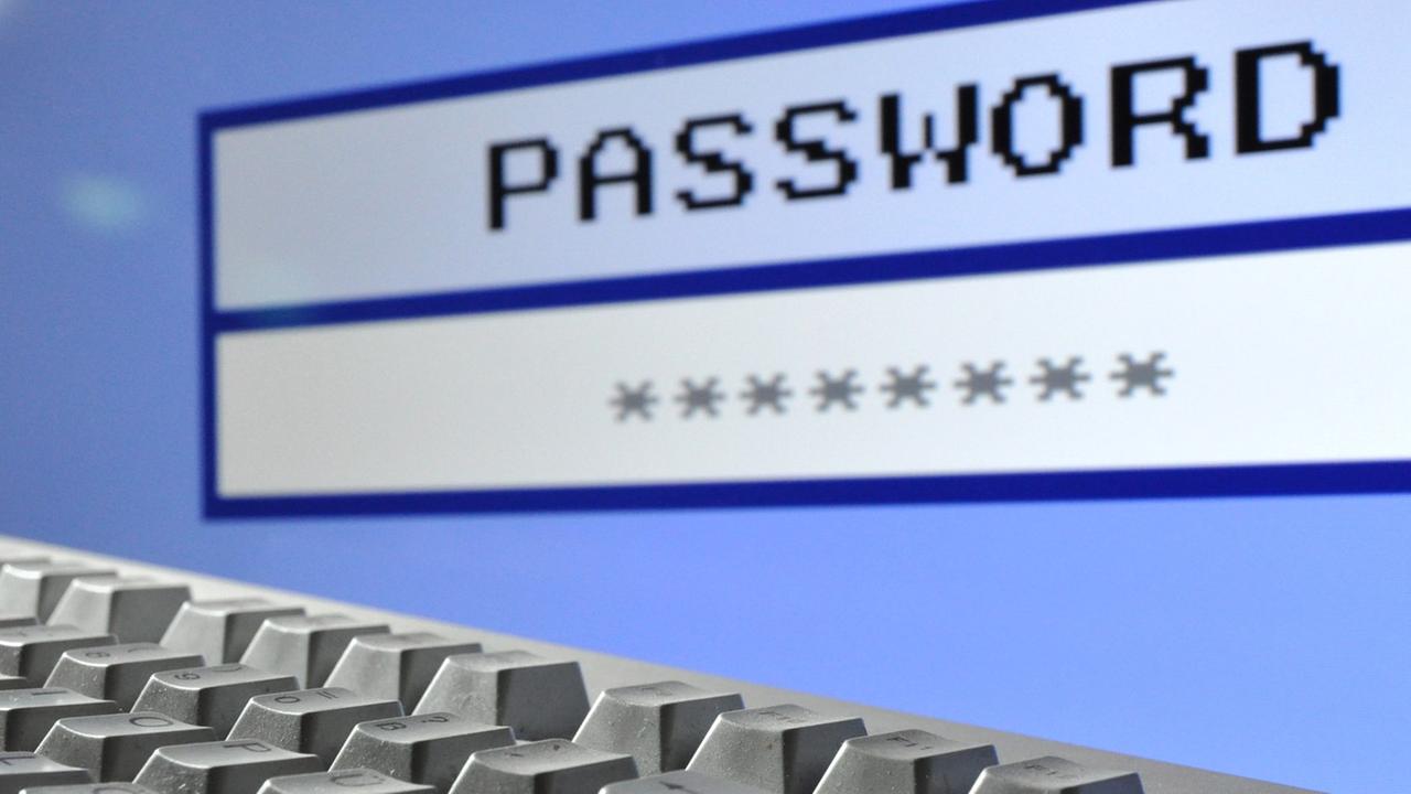 Eine Computertastatur. Im Hintergrund auf dem Bildschirm ist eine Passwortabfrage zu sehen. Eine Computertastatur. Im Hintergrund auf dem Bildschirm ist eine Passwortabfrage zu sehen.