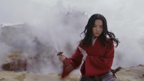 Schauspielerin Yifei Liu steht in der Rolle der Mulan in einer nebligen Landschaft. Sie nimmt eine Kämpferpose ein.