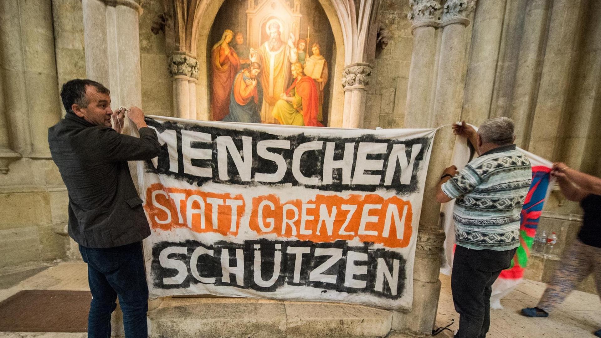 Flüchtlinge hängen am 06.07.2016 im Dom St. Peter in Regensburg (Bayern) ein Transparent mit der Aufschrift "Menschen statt Grenzen schützen" auf. Flüchtlinge hängen am 06.07.2016 im Dom St. Peter in Regensburg (Bayern) ein Transparent mit der Aufschrift "Menschen statt Grenzen schützen" auf.