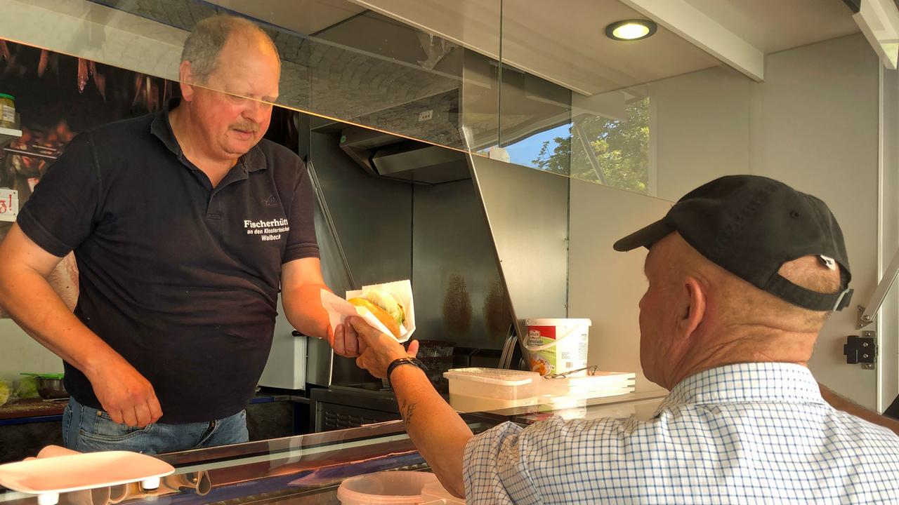 Der Fischhändler reicht einem Kunden die Ware. Der Fischhändler reicht einem Kunden die Ware.