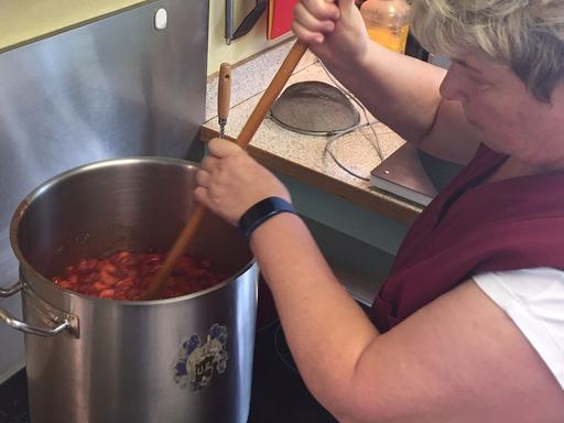 Anita Strauch rührt mit einem langen Holzlöffel in einem hohen Topf, in dem Erdbeeren und Zucker gekocht werden.