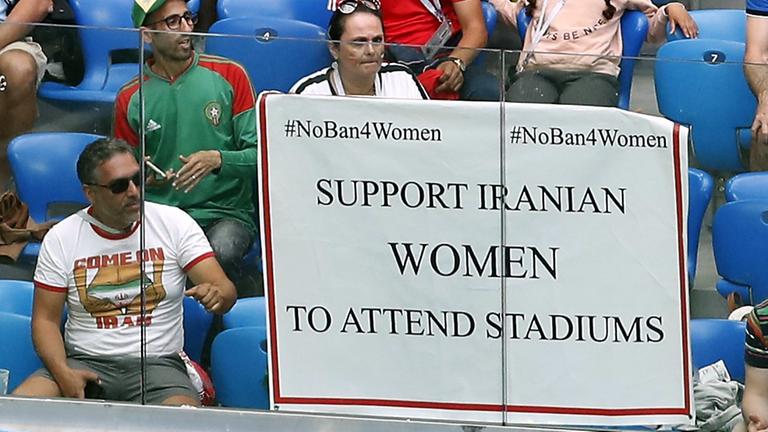 Das Bild zeigt eine Szene am Rande der Fußball-WM-Vorrundenbegegnung zwischen Marokko und dem Iran im Sankt-Petersburg-Stadion. Ein Poster zur Unterstützung von iranischen Frauen zum Besuch in Fußball-Stadien hängt an der Tribüne. Das Bild zeigt eine Szene am Rande der Fußball-WM-Vorrundenbegegnung zwischen Marokko und dem Iran im Sankt-Petersburg-Stadion. Ein Poster zur Unterstützung von iranischen Frauen zum Besuch in Fußball-Stadien hängt an der Tribüne.