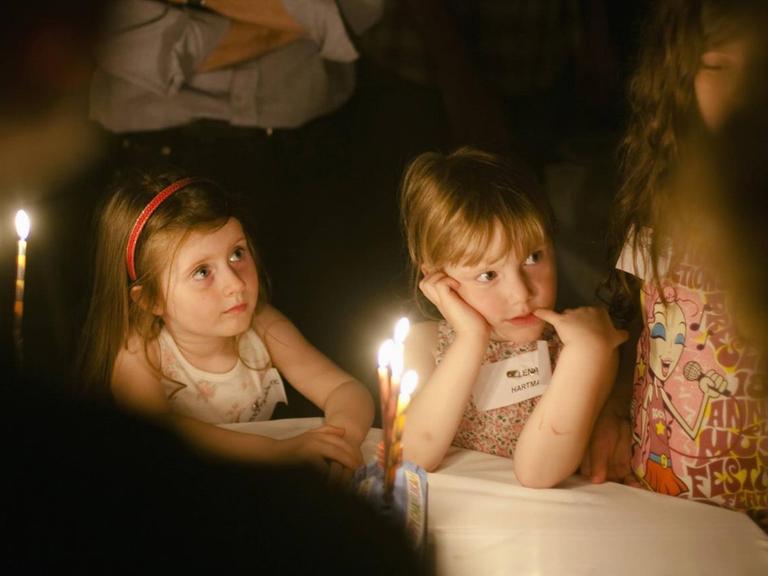 Kinder sitzen um einen Tisch und beobachten, wie die Kerzen zum jüdischen Lichterfest Chanukka angezündet werden.