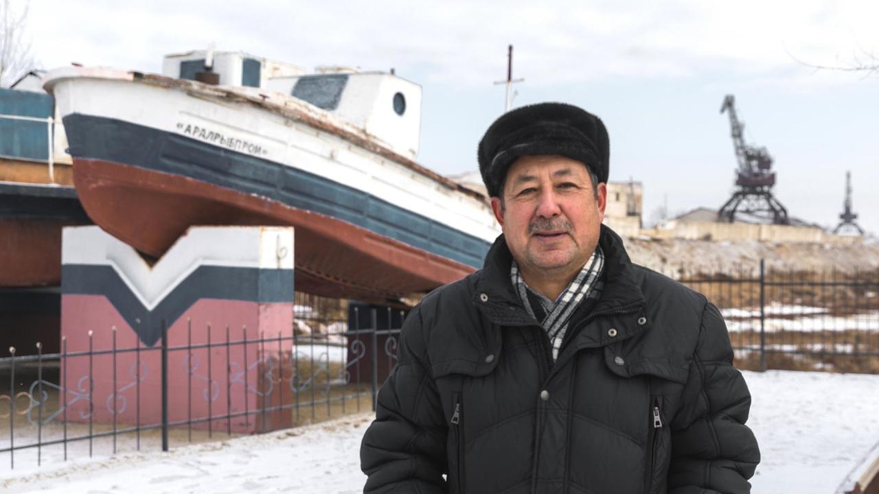 Museumsdirektor Madi Zhasekenov am früheren Hafen von Aralsk. Im Hintergrund sind alte Schiffe aufgestellt.