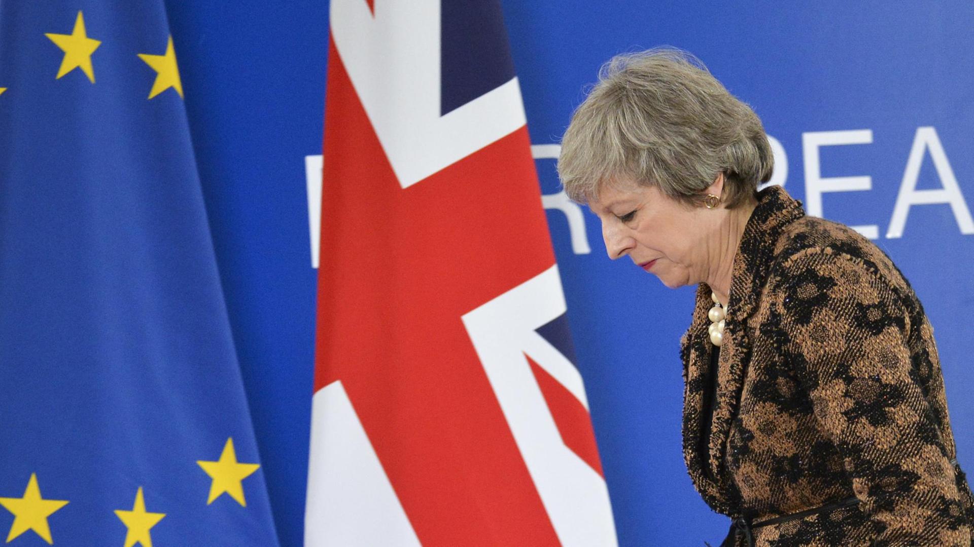 May läuft gebeugt an einer EU- und einer Gr0ßbritannien-Flagge vorbei. May läuft gebeugt an einer EU- und einer Gr0ßbritannien-Flagge vorbei.