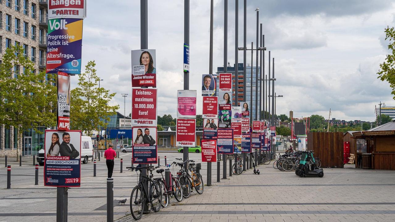 Auf einem Platz erstrecken sich viele Laternenmaste in die Höhe, an denen viele Wahlplakate hängen. Auf einem Platz erstrecken sich viele Laternenmaste in die Höhe, an denen viele Wahlplakate hängen.