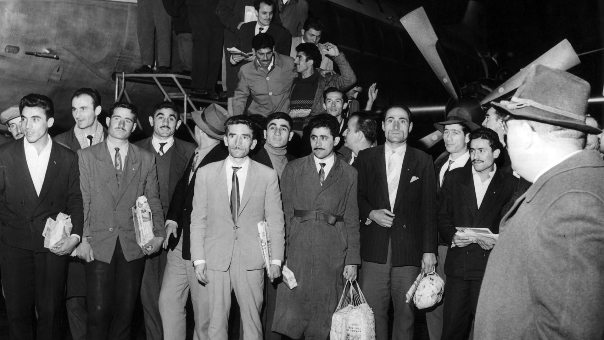 55 türkische Gastarbeiter kommen am 27.11.1961 auf dem Flughafen in Düsseldorf an. Im Hintergrund ist das Flugzeug zu sehen, in dem sie gelandet sind.