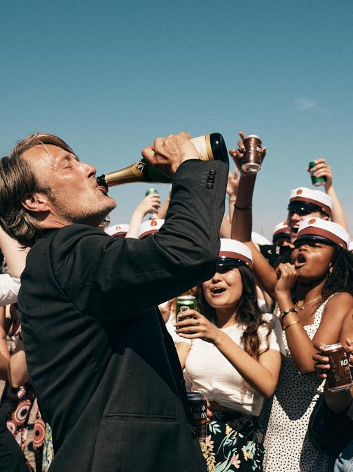 Der Schauspieler Mads Mikkelsen in einem Szenenfoto von Thomas Vinterbergs Film "Der Rausch". Mikkelsen trinkt aus einer Champagnerflasche.