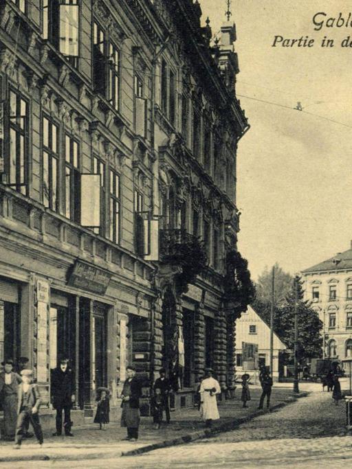 Historische Stadtansicht von Gablonz an der Neiße: Stadthäuser säumen eine Straße mit Kopfsteinpflaster, über die eine Straßenbahn fährt.