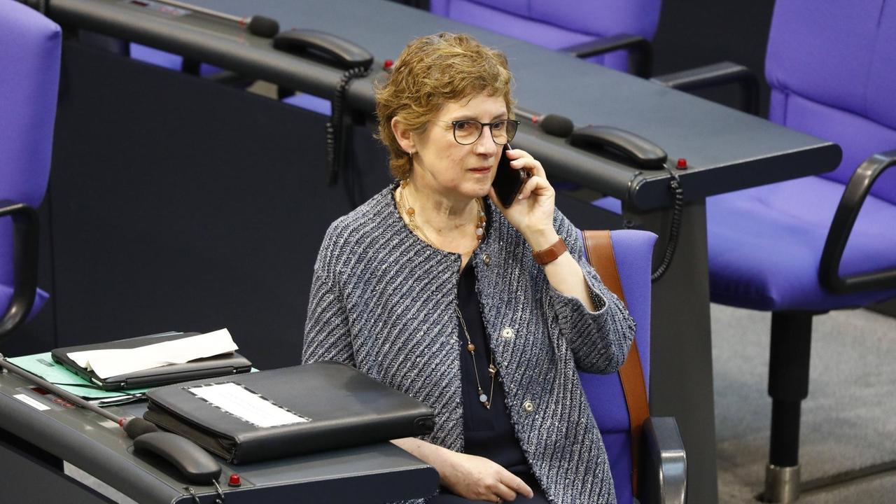 Die Parlamentarische Geschäftsführerin der Grünen im Bundestag, sitzt im Plenarsaal des Bundetags auf einem blauen Sessel und telefoniert mit einem Handy.